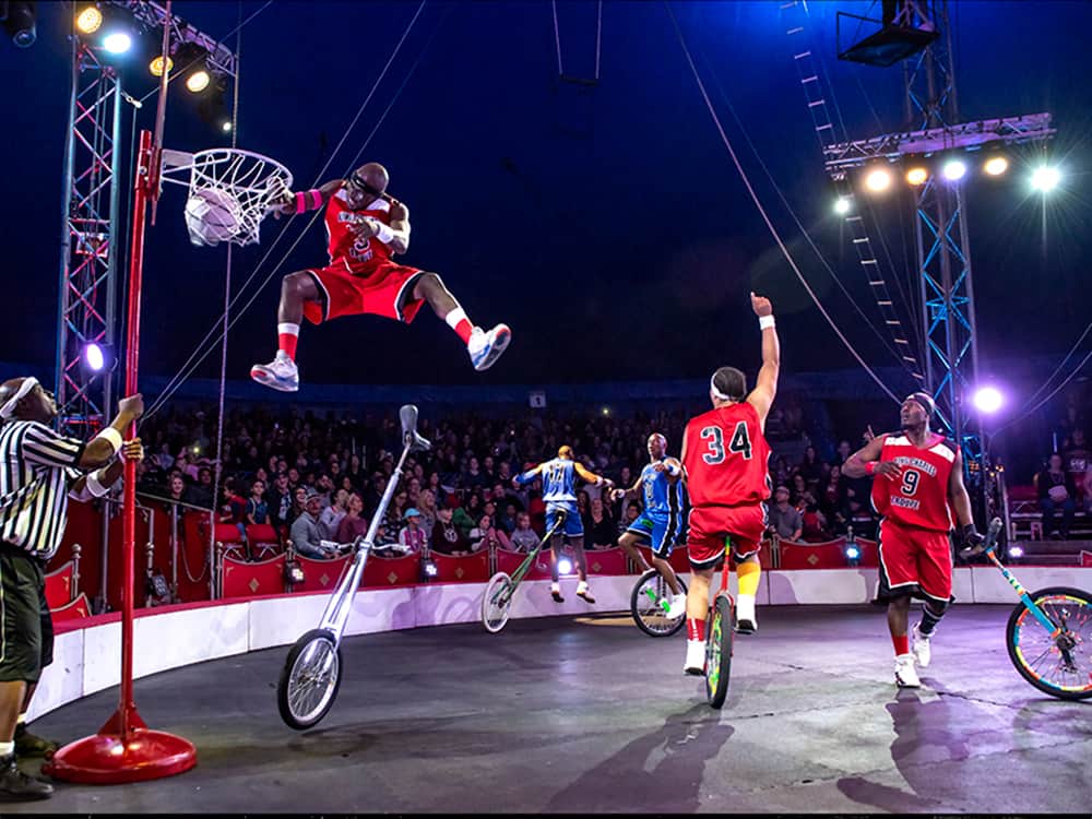 A group of men on unicycles playing basketball