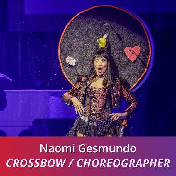 Naomi Gesmundo: Crossbow/Choreography , a tan woman with dark hair wearing a black and red costume standing in front of a target with an apple on her head; her mouth is wide in amazement as the arrow hits the Apple.