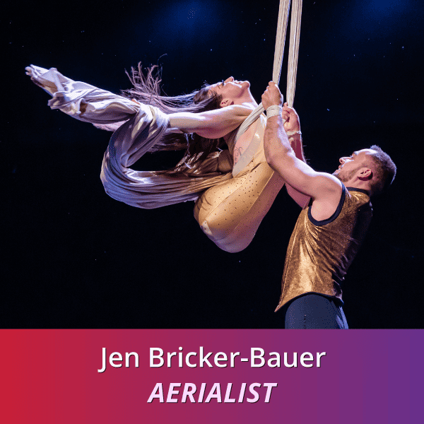 Jen Bricker-Bauer: Aerialist, a Caucasian woman born without legs who is wearing gold as she soars through the sky using Aerial Silks dancing mid air with her husband and partner Dominik who is also grasping the sliks