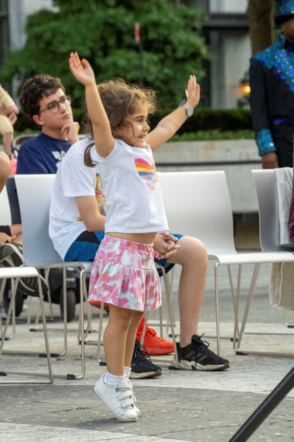 a young girl in the audience raises her arms in excitement.