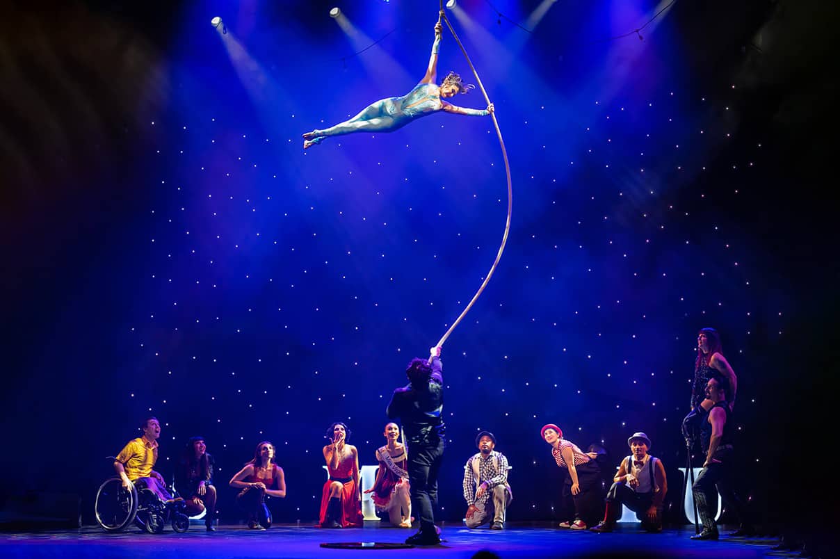 An aerialist performs as troupe members look on.