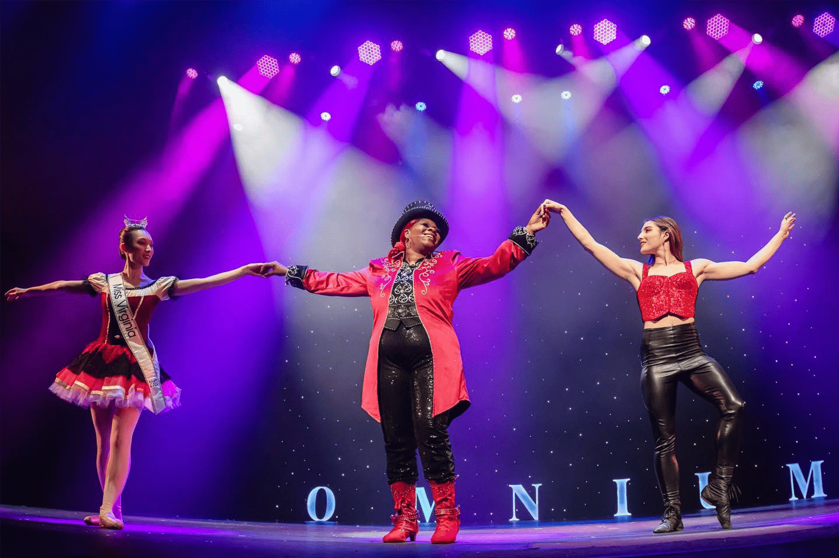 A ringmaster and two women on either side her prepare to take a bow.